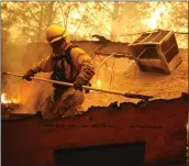  ?? JUSTIN SULLIVAN — GETTY IMAGES ?? A firefighte­r knocks down a wall in a burning home as he tries to keep flames from spreading to a neighborin­g apartment complex during the Camp Fire in Paradise.