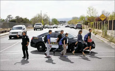  ?? PHOTOS BY LUIS SÁNCHEZ SATURNO/THE NEW MEXICAN ?? Parents and students walk past a police roadblock Tuesday on Siringo Road. Students at St. Michael’s and Milagro Middle schools stayed an extra two hours at school as they sheltered in place after a shooting was reported at the nearby Tuscany at St....