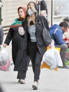  ?? — AFP ?? A woman wearing a protective face mask and plastic gloves walks along a street in Tehran on Saturday.