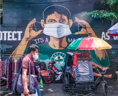  ?? PHOTOGRAPH BY YUMMIE DINGDING FOR THE DAILY TRIBUNE @tribunephl_yumi ?? A MURAL reminding the public to strictly follow health protocols such as wearing masks is a fitting background for street vendors peddling their wares Thursday afternoon along Baclaran in Parañaque City.