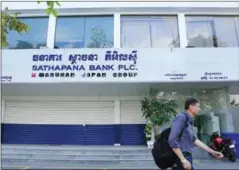  ?? PHA LINA ?? A man passes the head office of Sathapana Bank in Phnom Penh last month, after the bank removed its corporate logo.