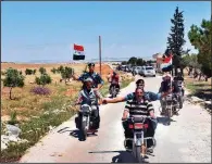  ?? AP/SANA ?? Syrian police officers join villagers in waving national flags Tuesday ahead of a convoy entering a village in northern Homs, which is now under government control.