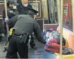  ?? JOHN MINCHILLO THE ASSOCIATED PRESS ?? New York City and transit police awake a sleeping passenger. The subways are closing nightly from 1 to 5 a.m. for disinfecti­ng during the COVID-19 pandemic.