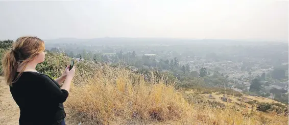  ?? ADRIAN LAM, TIMES COLONIST ?? Cassandra Felker takes a photo atop Mount Tolmie on Tuesday afternoon as smoke from wildfires obscures a panoramic view of Greater Victoria.