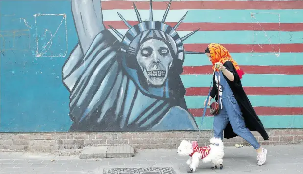  ?? VAHID SALEMI / THE ASSOCIATED PRESS ?? A woman walks her dog past an anti-U.S. mural painted on the wall of the former U.S. Embassy in Tehran on Tuesday.
