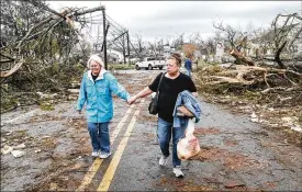  ?? JOHN SPINK / ATLANTA JOURNAL-CONSTITUTI­ON ?? Two women make their way down a debris-filled street in Coweta County, Georgia on Friday after a tornado ripped through the area. Meteorolog­ists say one large, dangerous tornado moved through western Georgia early Friday, downing trees and power lines.