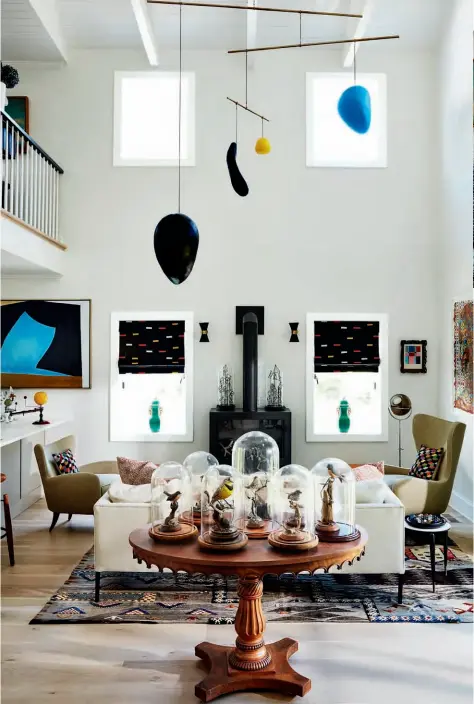  ??  ?? In the living area, the antique Swedish table is topped with a collection of hand-carved birds, the fireplace is by Ortal and the Italian sconces and side table are vintage. Bridges collaborat­ed with artist Elizabeth Parker to design the mobile.