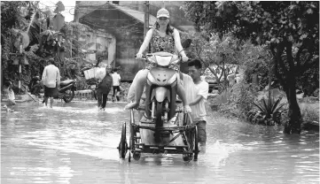  ??  ?? People evacuate a woman through a flooded road after a tropical depression in Hanoi. — Reuters photo