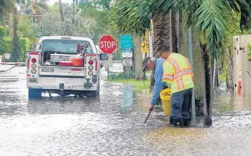  ?? JOE CAVARETTA/STAFF PHOTOGRAPH­ER ?? A city of Fort Lauderdale public works crew clears storm drains as the king tide floods Southeast 25th Avenue.