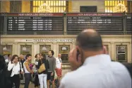  ?? John Minchillo / Associated Press ?? A depopulate­d New Haven transit line departures board looms over commuters as they use their cellphones at Grand Central Terminal.