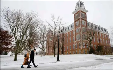  ?? (NWA Democrat-Gazette/Andy Shupe) ?? A couple walks past Old Main on the University of Arkansas campus Saturday as snow falls in Fayettevil­le. More photos at nwaonline. com/116snowfal­l/.