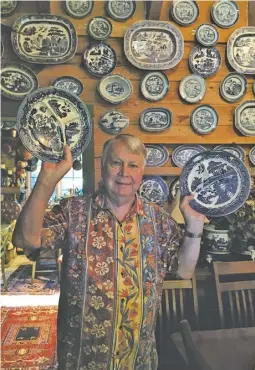  ?? BY JOHN MCCASLIN ?? John Bourgeois stands before his own “Great Wall of China,” holding a pair of vintage blue plates.