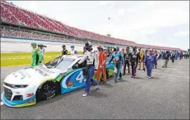  ?? John Bazemore Associated Press ?? KYLE BUSCH, far left, and Corey LaJoie, right, lead fellow drivers as they push Bubba Wallace’s car to the front of the field before the start of Monday’s race.
