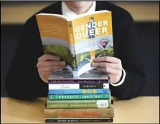  ?? ASSOCIATED PRESS ?? Amanda Darrow, director of youth, family and education programs at the Utah Pride Center, poses on Dec. 16, 2021, in Salt Lake City with books that have been the subject of complaints from parents.