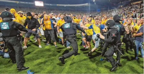  ??  ?? Nach dem Abpfiff stürmen Braunschwe­iger Chaoten das Spielfeld. Die Polizei verhindert, dass der pöbelnde Mob die Wolfsburge­r Fans angreifen kann.