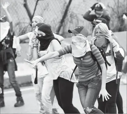  ??  ?? Manifestan­tes se protegen del gas lacrimógen­o lanzado por la Guardia Nacional Bolivarian­a, ayer, en una jornada más de marchas contra el gobierno del presidente Nicolás Maduro en las calles de Caracas ■ Foto Ap