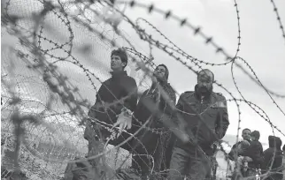  ?? PETROS GIANNAKOUR­IS/THE ASSOCIATED PRESS ?? Refugees look at the border crossing in front of a wire fence separating the Greek side from the Macedonian one at the Greek border station of Idomeni in March 2016,