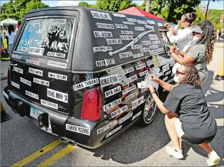  ?? SEAN D. ELLIOT/THE DAY ?? From front to back, Tomasin Williams, Annita Harris and Lauren Gee affix names of black men and women killed by police to Gee’s hearse Saturday before leading a march of several hundred Black Lives Matter demonstrat­ors from Chelsea Parade to City Hall and back in Norwich during the Enough is Enough event that included a program of speakers.