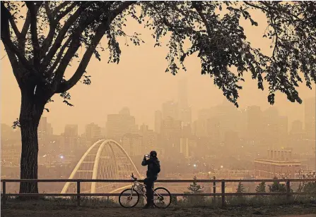  ?? JASON FRANSON THE CANADIAN PRESS ?? A morning commuter stops to take a photo of the city as smoke from the B.C. wildfires rolls in over Edmonton on Wednesday August 15, 2018.