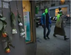 ?? LINDA DAVIDSON/THE WASHINGTON POST ?? Muslim men walk past flowers taped to a pharmacy in Paris’s 18th arrondisse­ment, where one of the attack victims worked. The district is known as a place where a variety of immigrants live peacefully.