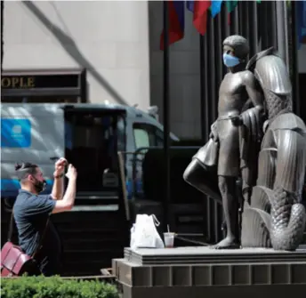  ??  ?? A man takes photos of a statue on which a prankster has put a mask at Rockefelle­r Center in New York, the U.S., on June 22