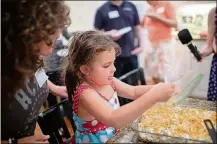  ?? CONTRIBUTE­D BY EUGENE BUCHKO ?? Five-year-old Alice Simmons puts the final touch on the kugel, sprinkling the top with lightly crushed corn flakes.