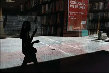  ?? Associated Press ?? ■ A passer-by holding a mobile device walks past a store window Tuesday in Cambridge, Mass. According to the Commerce Department U.S. retail sales jumped by a record 17.7% from April to May, with spending partially rebounding after the coronaviru­s had shut down businesses, flattened the economy and paralyzed consumers during the previous two months.