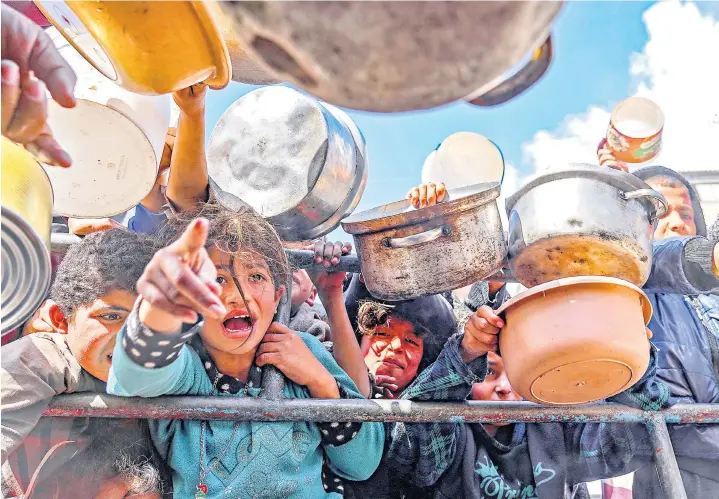  ?? ?? Palestinia­n children in Rafah wait in line to receive food prepared by volunteers