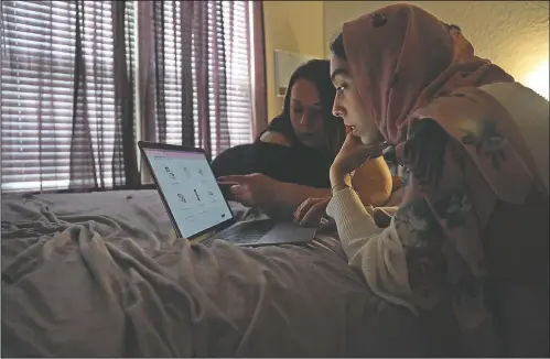  ?? (AP/Jessie Wardarski) ?? Angela Ahmed (left), and daughter Amirah Ahmed, 17, lie on a bed while browsing the internet Aug. 14 in Fredericks­burg, Va.