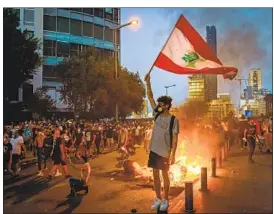  ?? Marcus Yam Los Angeles Times ?? A PROTESTER raises a Lebanese f lag during an Aug. 4 march toward parliament to mark the anniversar­y of the port explosion that killed more than 200.