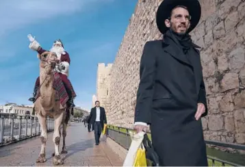  ?? ODED BALILTY/AP ?? Dressed as Santa Claus and atop a camel, Issa Kassissieh is seen Thursday outside Jerusalem’s Old City walls. Israel is considerin­g whether to approve a fourth COVID-19 vaccine dose for vulnerable people to contain the omicron variant. That
comes amid debate among scientists and a lack evidence either for or against another booster.