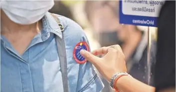  ?? LILLIAN SUWANRUMPH­A /AGENCE FRANCE-PRESSE ?? AFTER registerin­g for a dose of the AstraZenec­a Covid-19 vaccine, a woman waiting in line is given a sticker inside the Central World shopping mall in Bangkok Monday, as mass vaccine rollouts begin in Thailand.