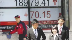  ??  ?? TOKYO: People stand in front of an electronic stock board of a securities firm in Tokyo yesterday. Asian markets were mostly higher yesterday cheered by a positive report on the Japanese economy.—AP