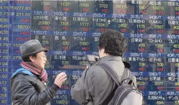  ?? — AFP ?? A pedestrian speaks to a television journalist in front of an electric quotation board flashing numbers of the Nikkei key index afternoon session of the Tokyo Stock Exchange in Tokyo.