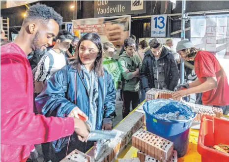  ?? FOTO: CHRISTIAN FLEMMING ?? Yusuf Abdirahman (links) zeigt geduldig, wie man den Mörtel richtig auf den Ziegeln verteilt, damit die nächste Lage richtig draufpasst. Der Club Vaudeville ist wieder Schauplatz für die diesjährig­e Handwerkso­ffensive der Kreishandw­erkskammer Lindau.