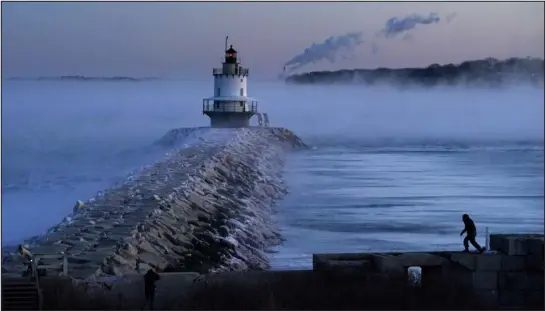  ?? PHOTOS BY ROBERT F. BUKATY — THE ASSOCIATED PRESS ?? A man walks on a sea wall near Spring Point Ledge Light on Saturday in South Portland, Maine. The morning temperatur­e was about minus 10 degrees.