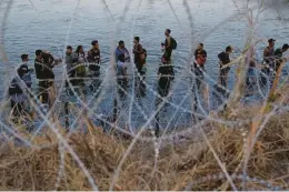  ?? ERIC GAY/AP 2023 ?? Migrants wait to climb over concertina wire in Eagle Pass, Texas, after they crossed the Rio Grande from Mexico. Texas’ new migrant law is on hold for nowss.
