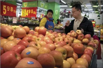  ??  ?? A woman wearing a uniform with the logo of an American produce company helps a customer shop for apples a supermarke­t in Beijing on Friday. China announced a $3 billion list of U.S. goods including pork, apples and steel pipe on Friday that it said may...