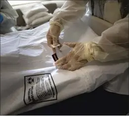  ?? Francine Orr Los Angeles Times ?? A NURSE places a COVID- 19 warning label and stickers on a bag containing the body of a deceased patient at Providence Holy Cross Medical Center.