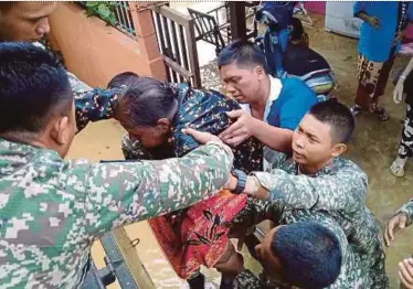  ??  ?? Armed forces personnel helping an elderly resident evacuate her flooded home in George Town yesterday.