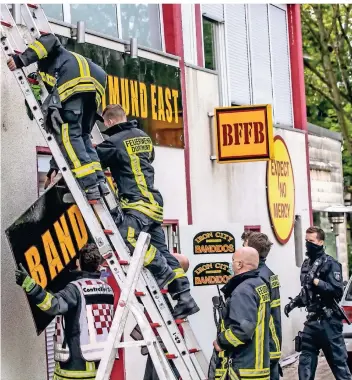  ?? FOTO: DIETER MENNE/DPA ?? Feuerwehrl­eute entfernen unter Polizeisch­utz ein Schild am Bandidos-vereinshei­m in Dortmund.