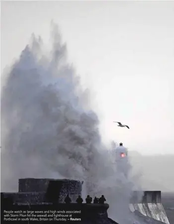  ?? — Reuters ?? People watch as large waves and high winds associated with Storm Ffion hit the seawall and lighthouse at Porthcawl in south Wales, Britain on Thursday.