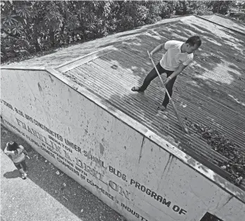  ?? MACKY LIM ?? CLEANING. A teacher climbs on top of a schoolbuil­ding to clear the roof of leaves during yesterday's Brigada Eskwela at Ma-a Central Elementary School where volunteers ensured a top to bottom clean-up before the start of classes.