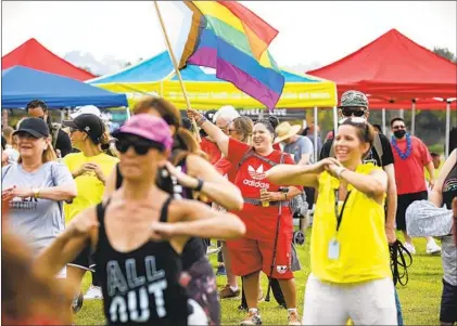  ?? NANCEE E. LEWIS PHOTOS ?? Hundreds of people, including Yolanda Ochoa holding a LGBTQ flag, warm up for the ninth annual 5K Walk for Sobriety on Saturday at Liberty Station’s NTC Park. Some participan­ts wore the number of days that they have been clean and sober.