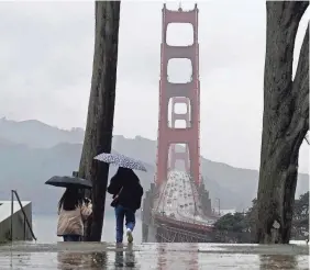  ?? JEFF CHIU, AP JEFF CHIU, AP ?? Traffic moves on the Golden Gate Bridge as people carry umbrellas while walking down a path at the Golden Gate Overlook in San Francisco, March 9, 2023. California is bracing for the arrival of an atmospheri­c river that forecaster­s warn will bring heavy rain, strong winds, thundersto­rms and the threat of flooding even as the state is still digging out from earlier storms.