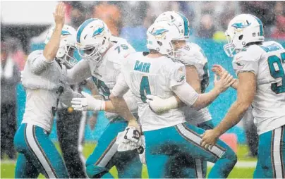  ?? PHOTOS BY JIM RASSOL/STAFF PHOTOGRAPH­ER ?? Dolphins kicker Andrew Franks, left, celebrates the winning field goal with teammates in the rain Sunday at Hard Rock Stadium.