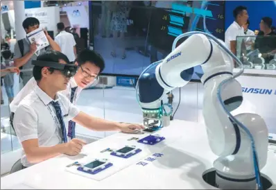  ?? AKASH GHAI / CHINA DAILY ?? Employees of Siasun Robot &amp; Automation Co use a robot and special eye gear to demonstrat­e phone repairs during the World Robot Conference held in Beijing on Wednesday.