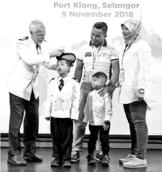  ??  ?? SuperStar Gemini captain Christian Westergren (left) affixing a captain’s cap on six-year-old leukaemia survivor Adam Khalish Harfa Azhar (second left) who is a special guest aboard with his parents car salesman Azahar Sojot and Fazidah Hassan, and his three-year-old brother Luth Harith. - Bernama photo