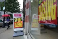  ?? Associated Press ?? ■ A passer-by walks past a business storefront with store closing signs Wednesday in Boston.