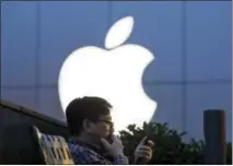  ?? NG HAN GUAN — THE ASSOCIATED PRESS FILE ?? In this Friday file photo, a man uses his mobile phone near an Apple store in Beijing. Apple reports financial results Tuesday.